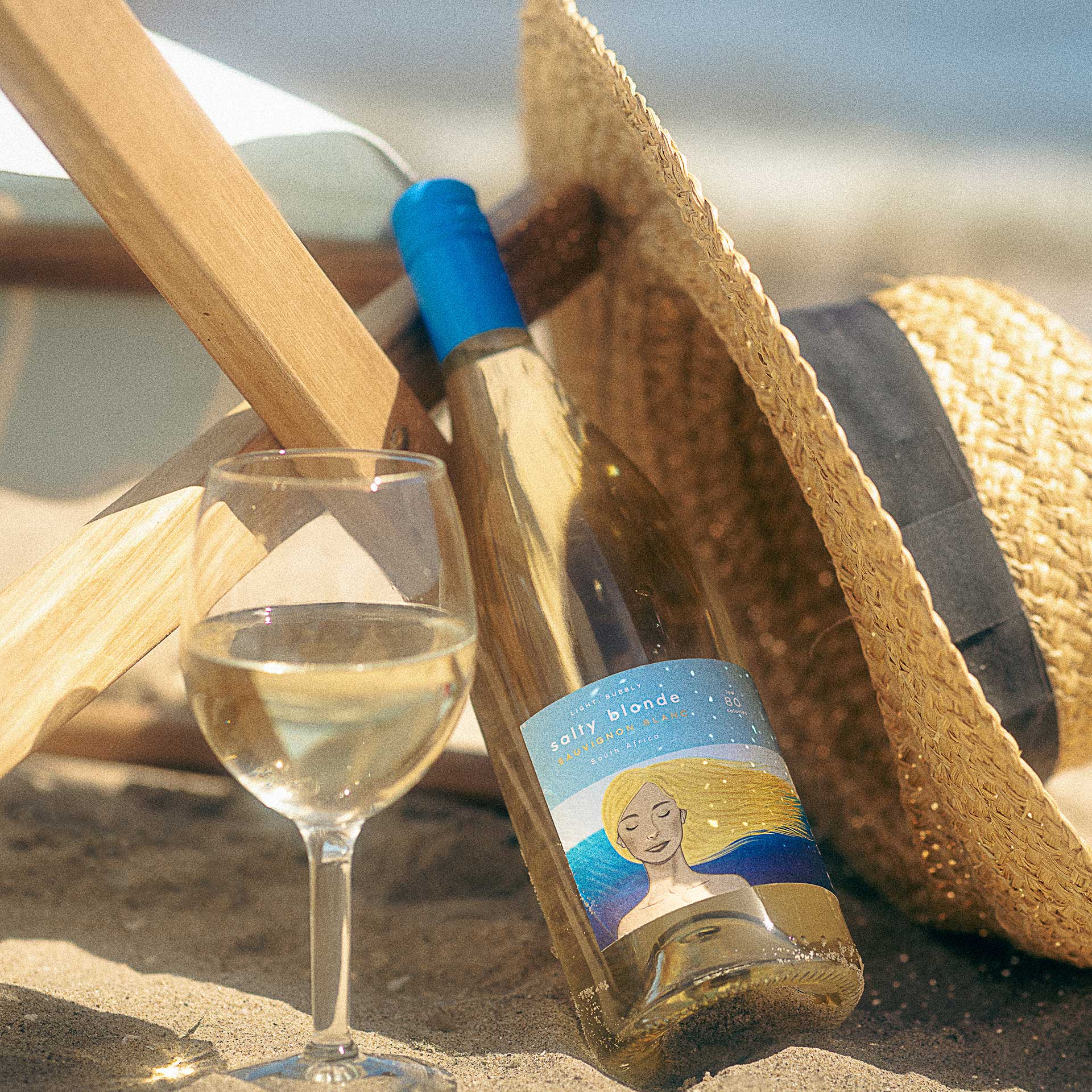 salty blonde wine bottle and glass with hat on sand