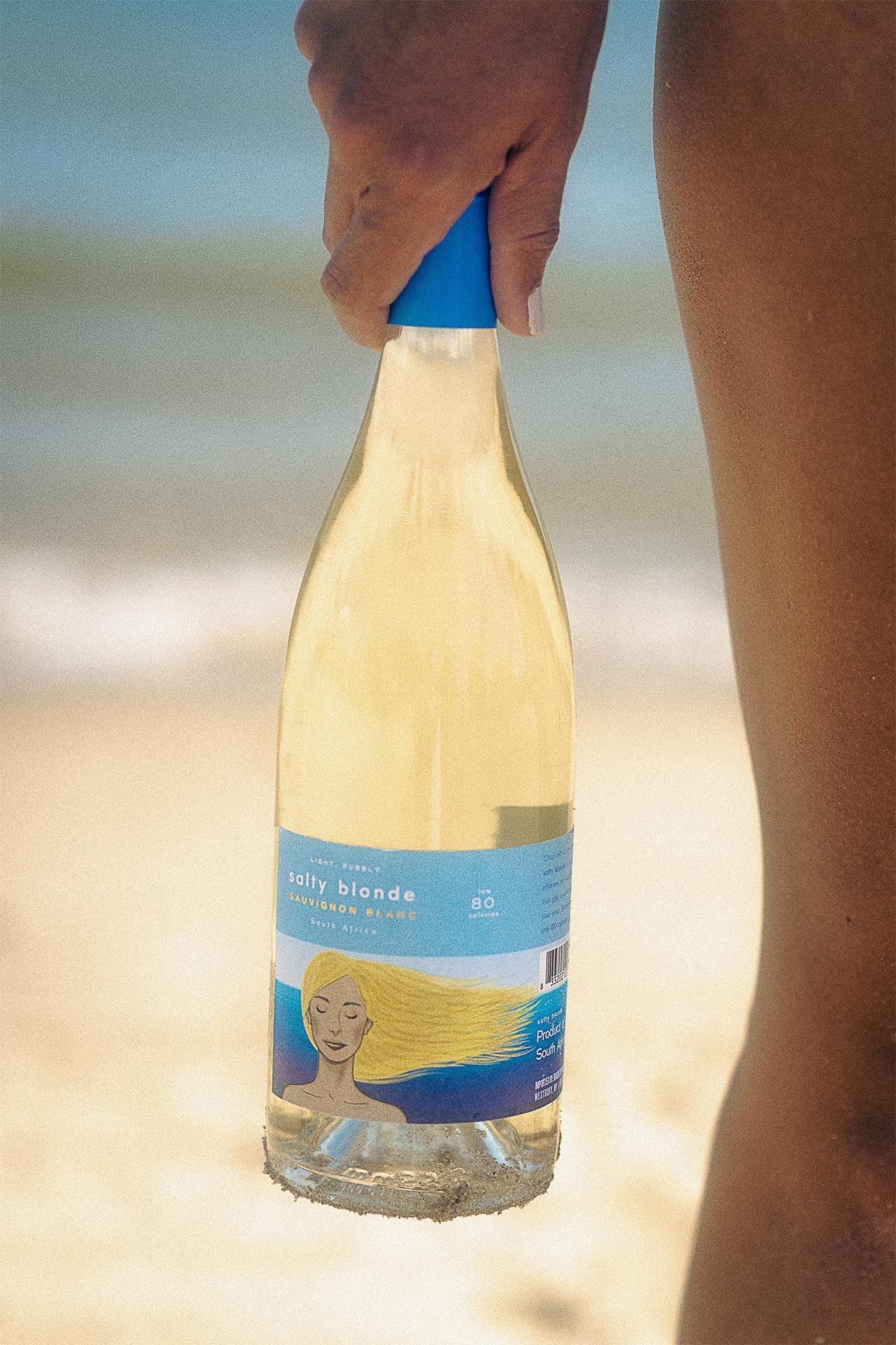 salty blonde wine bottle in woman's hand at beach